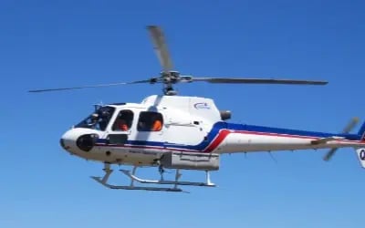 A while helicopter with blue and red stripes flying on a clear day