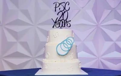 A three-tiered white cake adorned with PSC's logo and a topper that reads, 